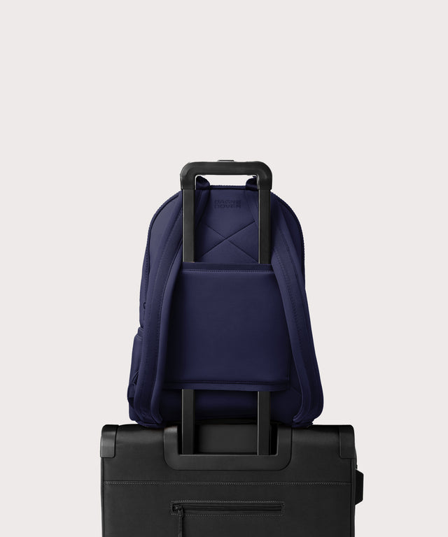 Dagne Dover large Dakota Neoprene Backpack in dark blue strapped to luggage with the neoprene luggage-handle sleeve.