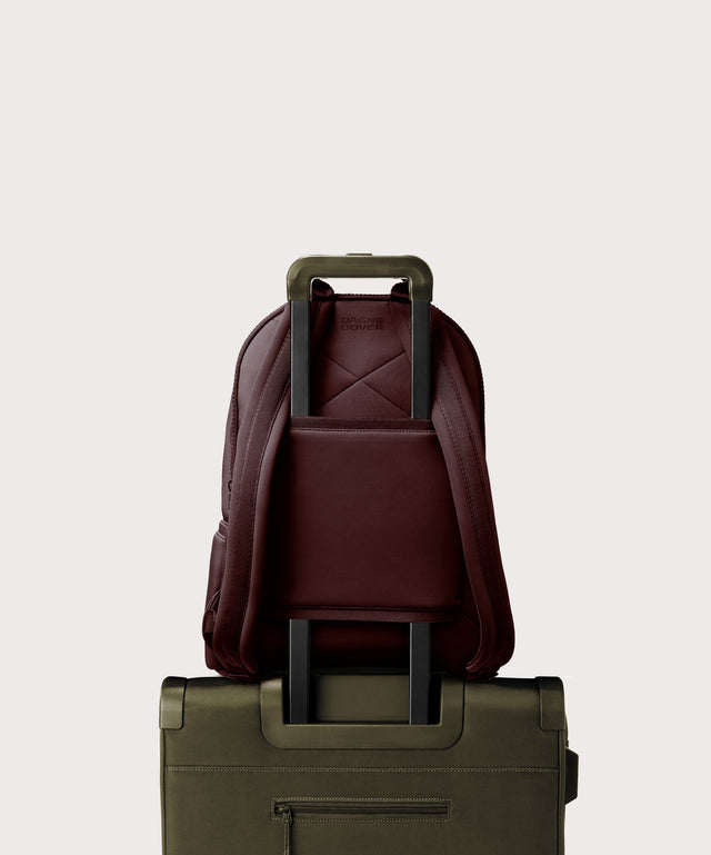 Dagne Dover Large Dakota Neoprene Backpack in a deep brown with purple undertones strapped to luggage with the neoprene luggage-handle sleeve.