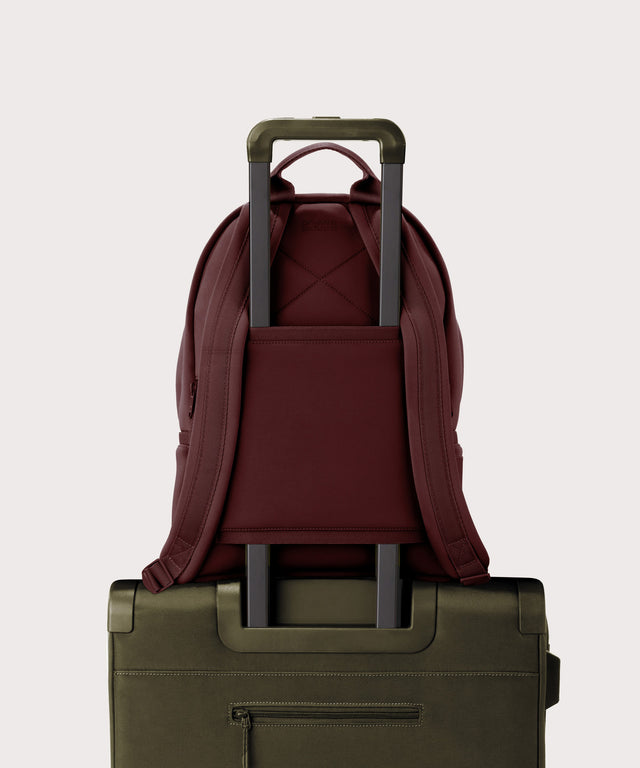 Dagne Dover Medium Dakota Neoprene Backpack in a deep brown with purple undertones strapped to luggage with the neoprene luggage-handle sleeve.