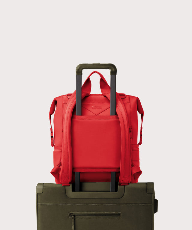 Dagne Dover Large Indi Diaper Backpack in a fiery, saturated red leaning toward orange on luggage, showing the luggage sleeve.