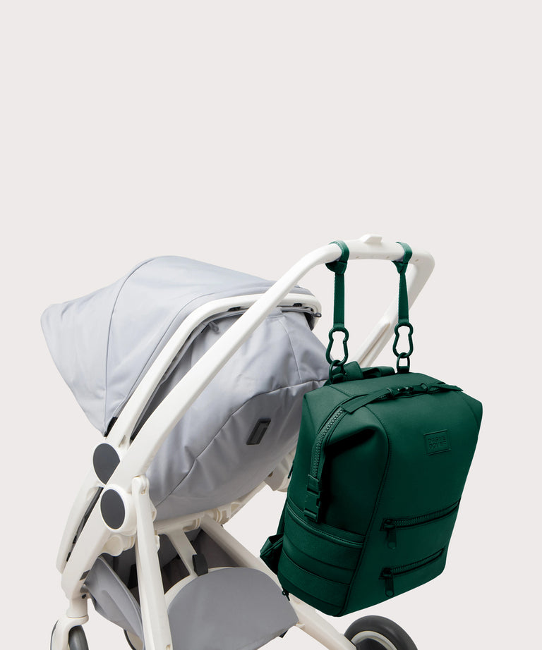 Large Indi backpack in a saturated, jewel-toned deep green with bold blue undertones. side angle view hanging on a stroller
