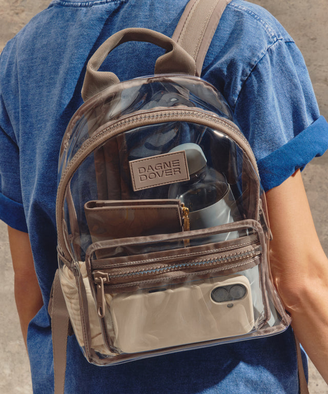 Person wearing a transparent backpack with beige straps and a visible brand logo.Stadium compliant. 