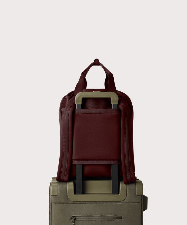 Rhys Backpack in a deep brown with purple undertones strapped to luggage with the neoprene luggage-handle sleeve.