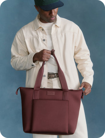 Man holding a maroon tote bag against a blue background