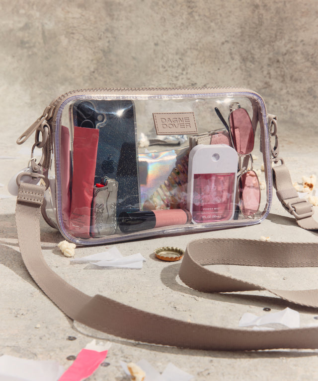 Clear cosmetic bag with visible contents and accessories on a textured surface. Stadium compliant. 