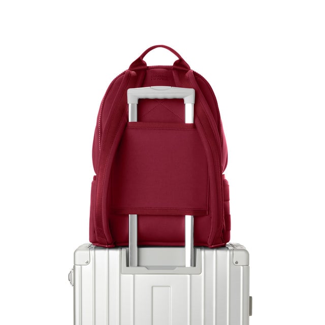 Dagne Dover large Dakota Neoprene Backpack in spice red strapped to luggage with the neoprene luggage-handle sleeve.