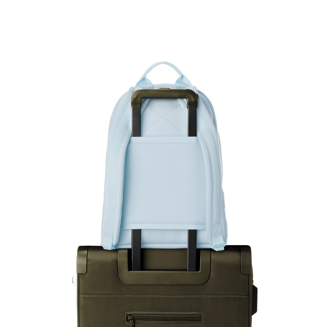 Dagne Dover medium Dakota Neoprene Backpack in an airy, lighter sky blue strapped to luggage with the neoprene luggage-handle sleeve.
