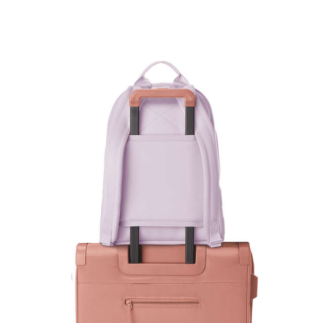 Dagne Dover medium Dakota Neoprene Backpack in a soft purple with grey undertones strapped to luggage with the neoprene luggage-handle sleeve.
