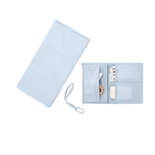hover - Dagne Dover Joey Changing Kit in an airy, lighter sky blue unfolded, revealing the interior zipper pocket and interior slip pockets.
