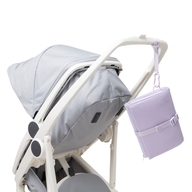 Dagne Dover Joey Changing Kit in a soft purple with grey undertones strapped to the handle of a stroller.
