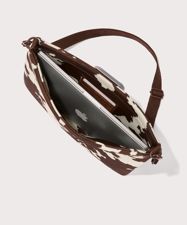 14 inch laptop shoulder bag in a cow print seen from the top down view. 
