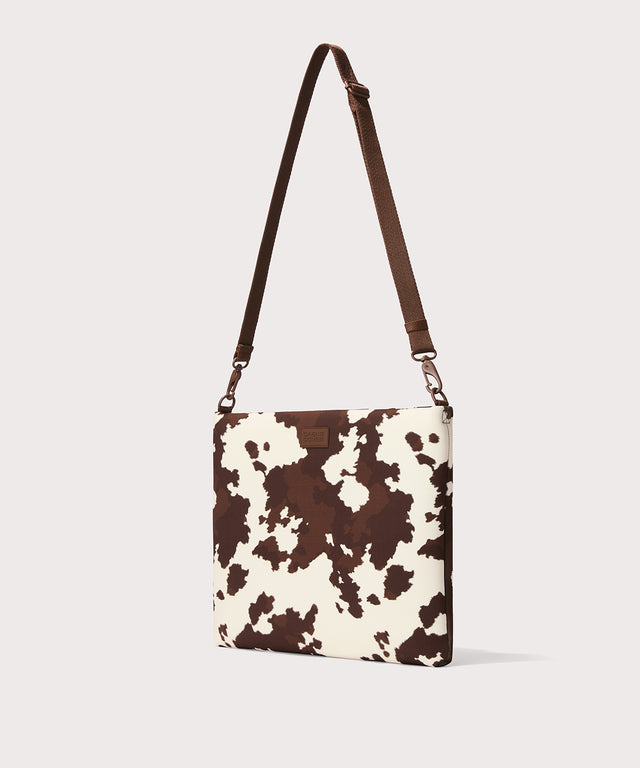 16 inch laptop shoulder bag in a cow print seen from the angle view. 
