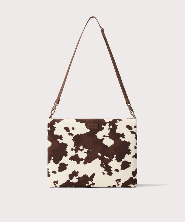 16 inch laptop shoulder bag in a cow print seen from the front view. 

