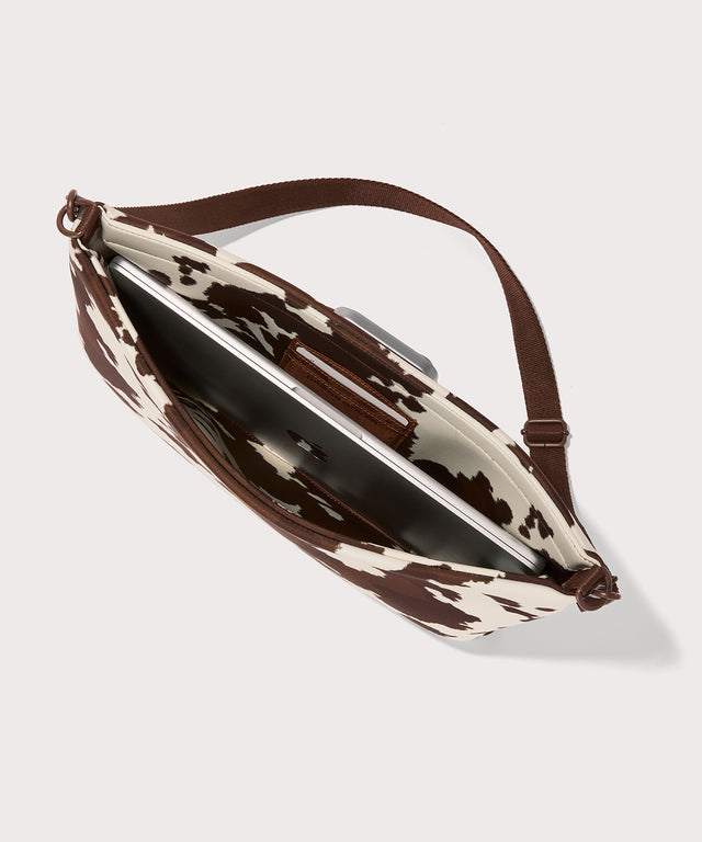 16 inch laptop shoulder bag in a cow print seen from the top down view. 
