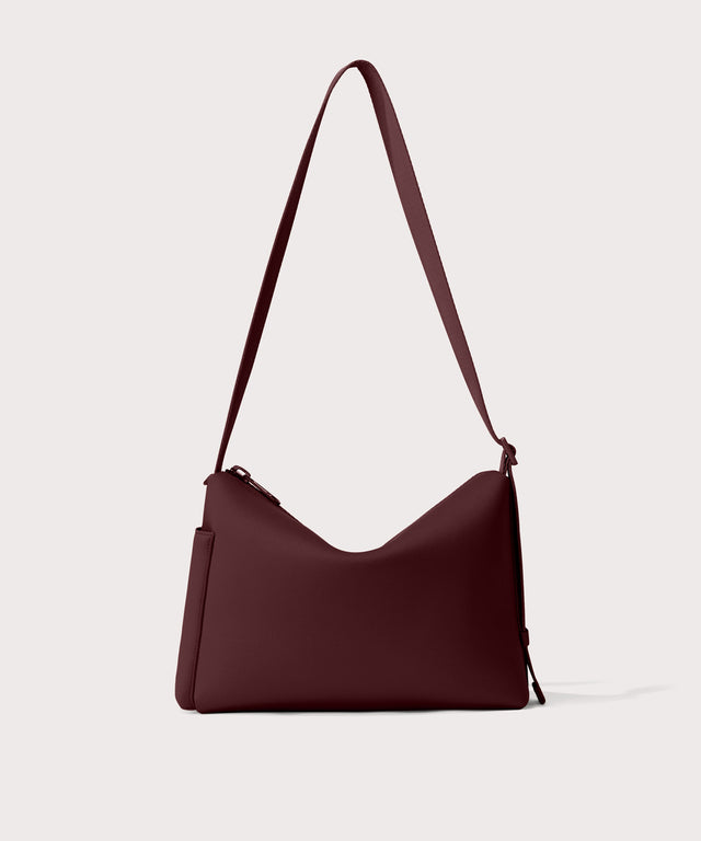 Shoulder bag in a fiery,  deep brown with purple undertones reminiscent of maroon seen from the back view showing phone pocket.