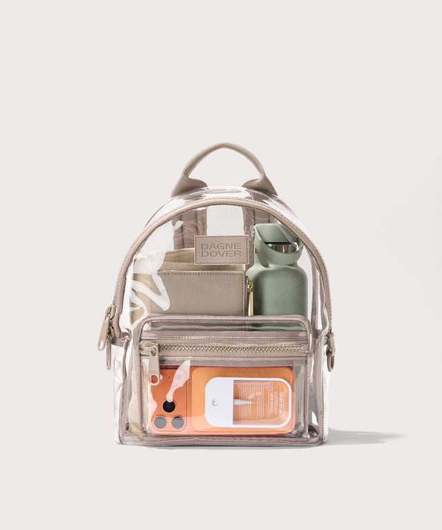 Clear backpack with beige straps and front pocket, holding various items on a white background. Stadium compliant. 
