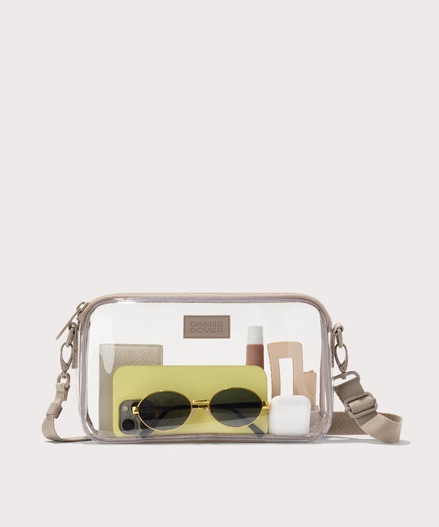 Clear crossbody bag with sunglasses, phone, and other accessories with a beige strap. Stadium compliant. 