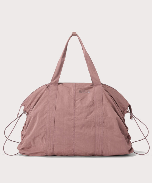 A dusty rose pink lightweight duffel bag with dual top handles, side drawstring details, and a small tonal logo on the front, shown against a light gray background.