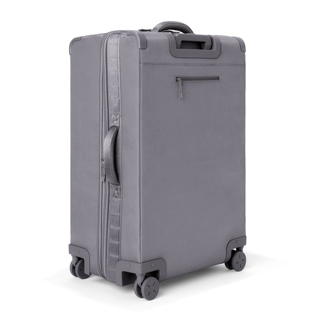 3/4 back view of Sydney checked rolling luggage 28.5” in ash grey showing side handle and back zippered phone/passport pocket