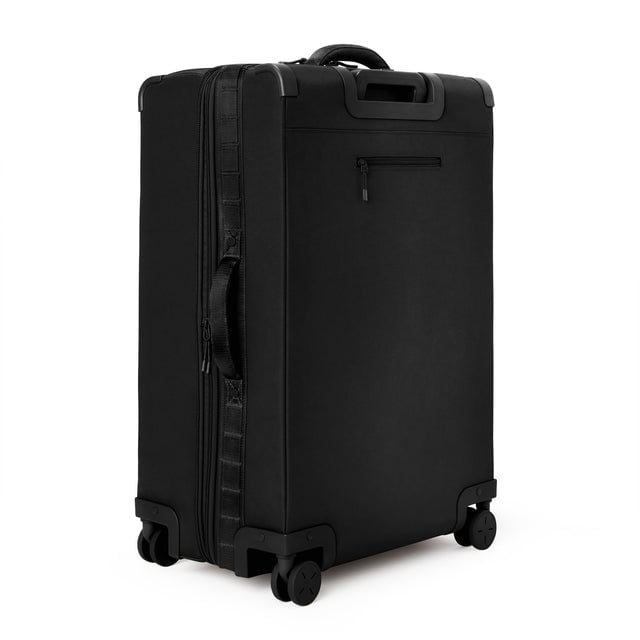 3/4 back view of Sydney checked rolling luggage 28.5” in onyx showing side handle and back zippered phone/passport pocket