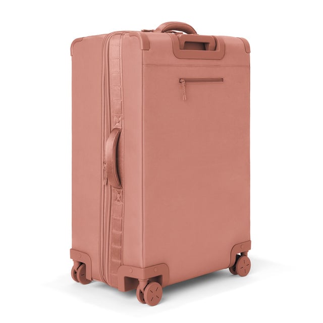 3/4 back view of Sydney checked rolling luggage 28.5” in warm dust showing side handle and back zippered phone/passport pocket
