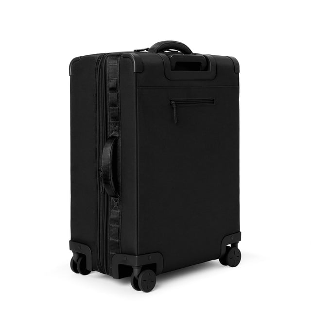 3/4 back view of Sydney checked rolling luggage 25” in onyx showing side handle and back zippered phone/passport pocket