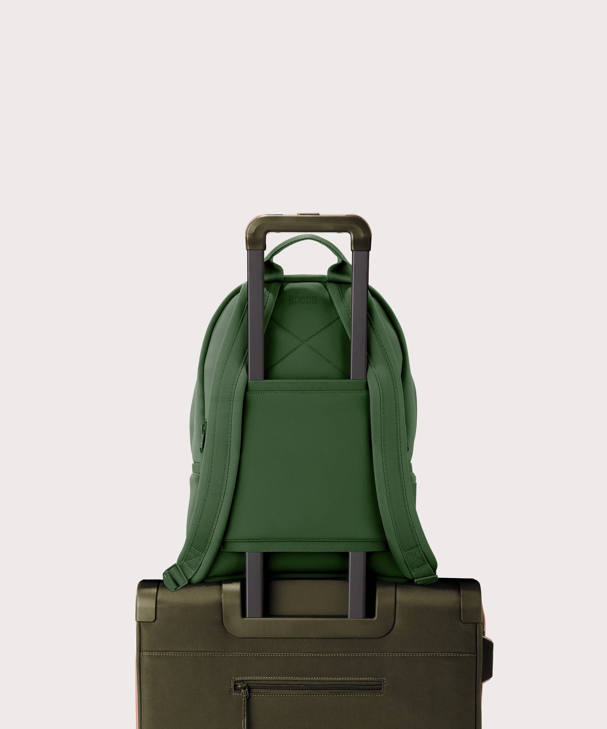 Dagne Dover medium Dakota Neoprene Backpack in a rich, classic forest green strapped to luggage with the neoprene luggage-handle sleeve.
