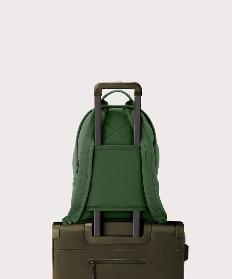 Dagne Dover medium Dakota Neoprene Backpack in a rich, classic forest green strapped to luggage with the neoprene luggage-handle sleeve.

