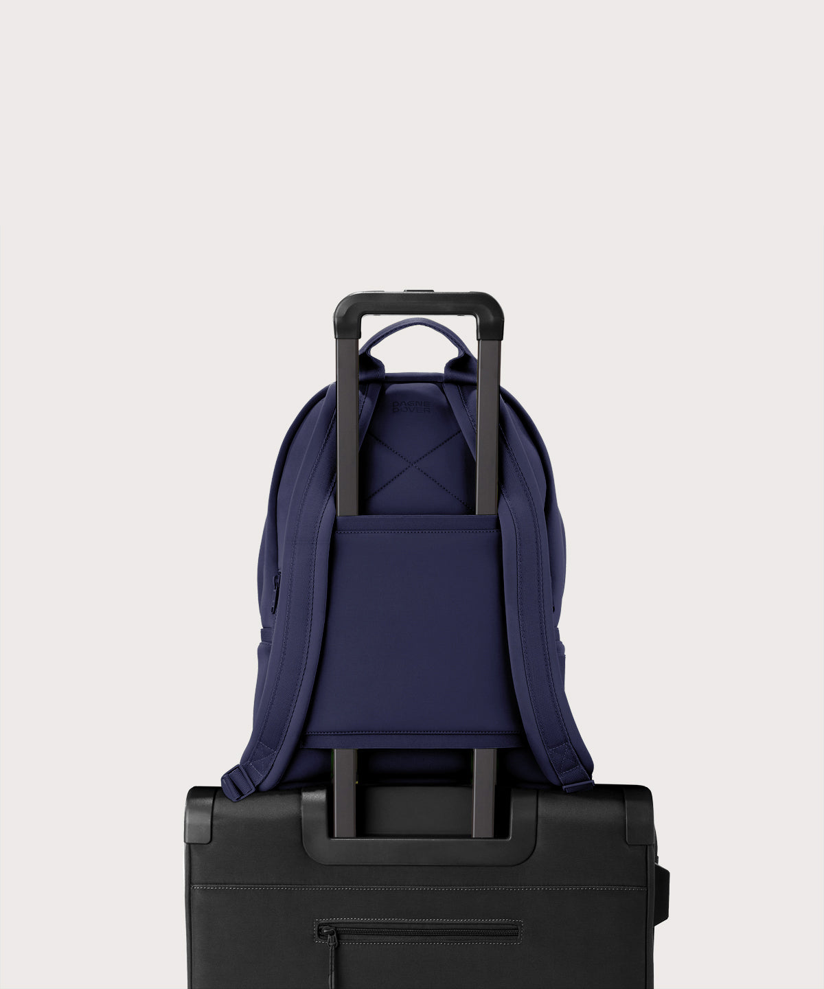 Dagne Dover medium Dakota Neoprene Backpack in dark blue strapped to luggage with the neoprene luggage-handle sleeve.
