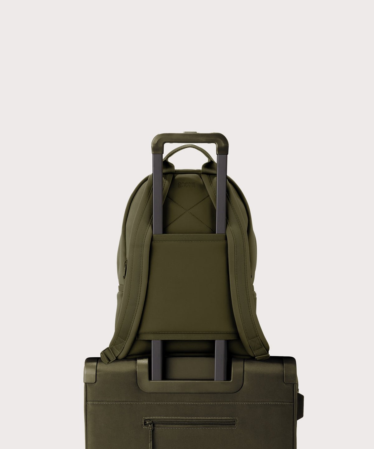 Dagne Dover medium Dakota Neoprene Backpack in dark moss strapped to luggage with the neoprene luggage-handle sleeve.
