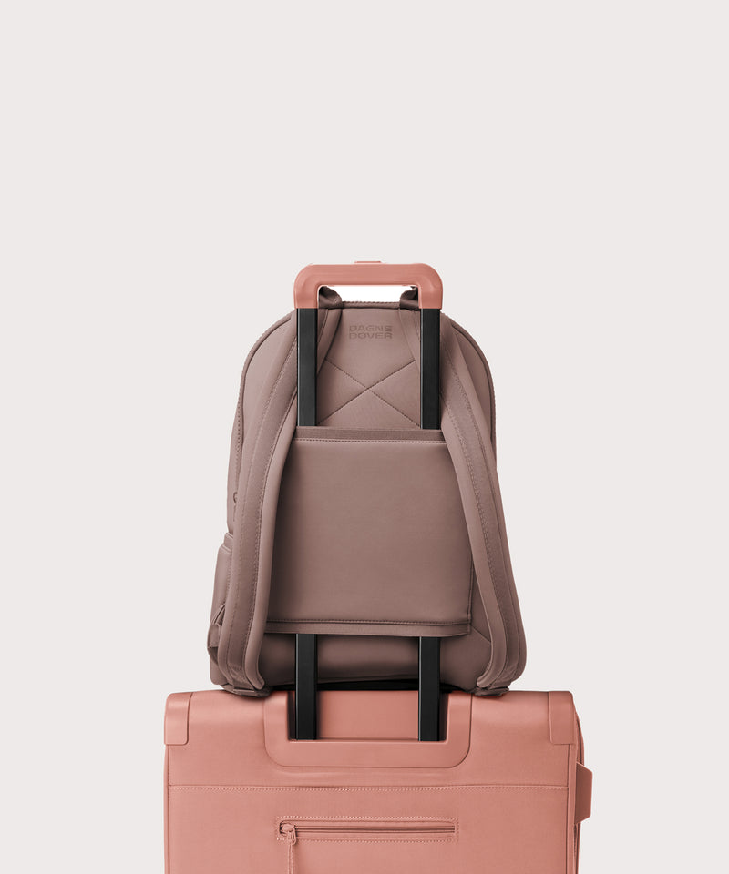 Dagne Dover medium Dakota Neoprene Backpack in pink strapped to luggage with the neoprene luggage-handle sleeve.
