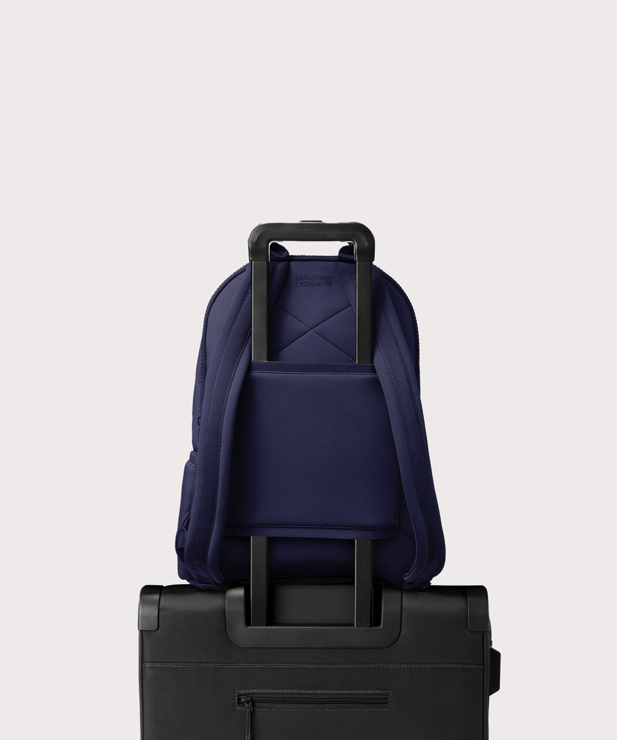 Dagne Dover large Dakota Neoprene Backpack in dark blue strapped to luggage with the neoprene luggage-handle sleeve.
