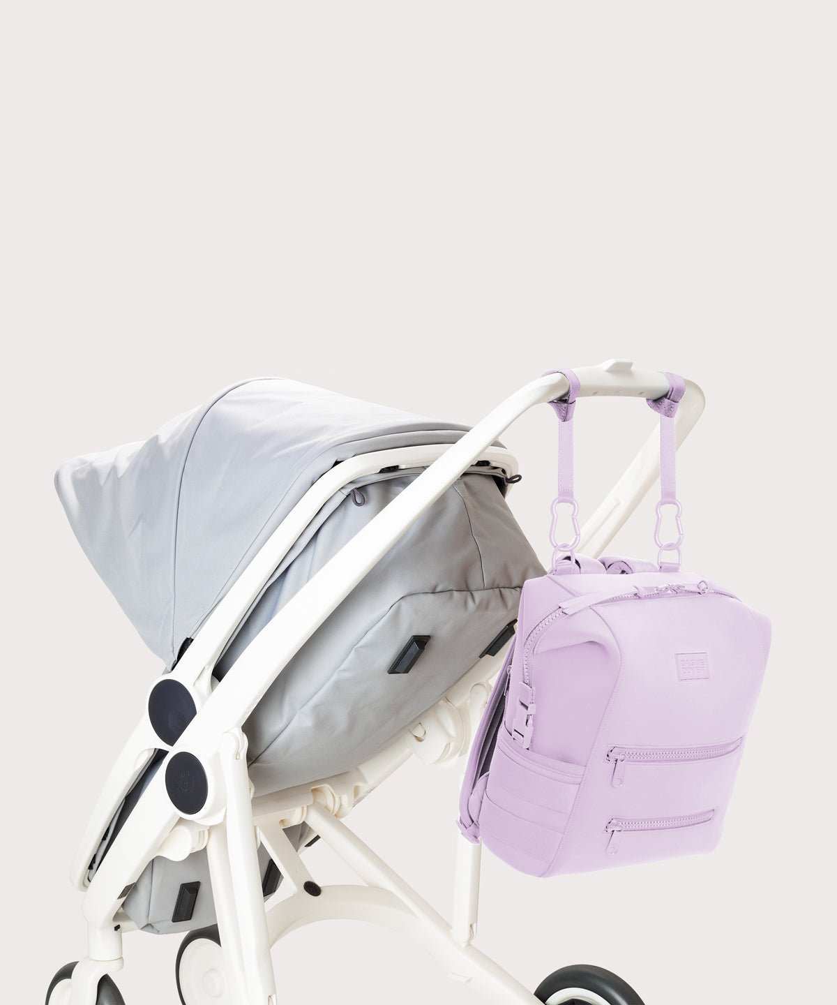 Dagne Dover Medium Indi Diaper Backpack in a soft purple with grey undertones attached to a stroller.
