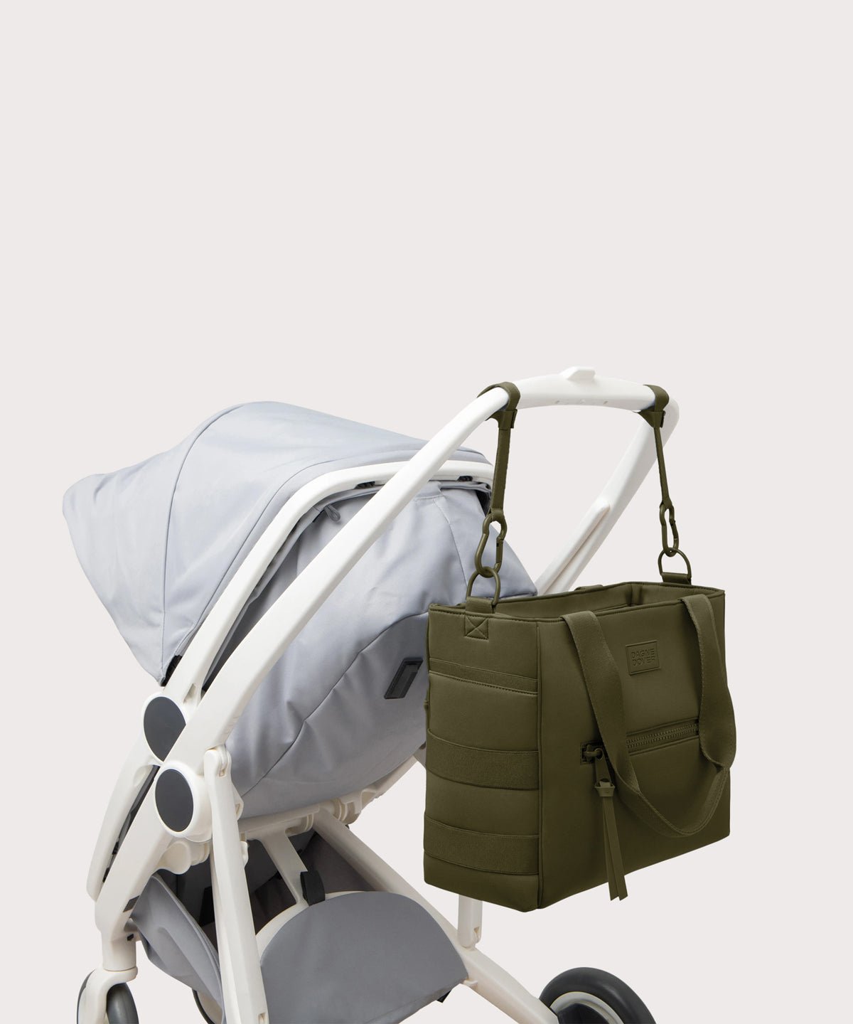 Dagne Dover large Wade Diaper Tote in dark green strapped to the handle of a stroller.
