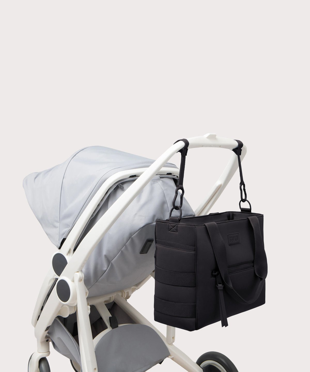 Dagne Dover large Wade Diaper Tote in black strapped to the handle of a stroller.
