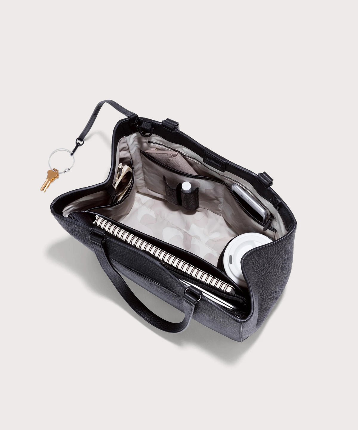 Dagne Dover medium Allyn Tote in black with objects inside the interior pockets.

