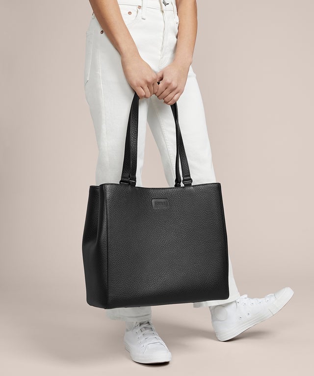 A model holding the 11.25 inch handle of the medium Allyn Tote in black. 
