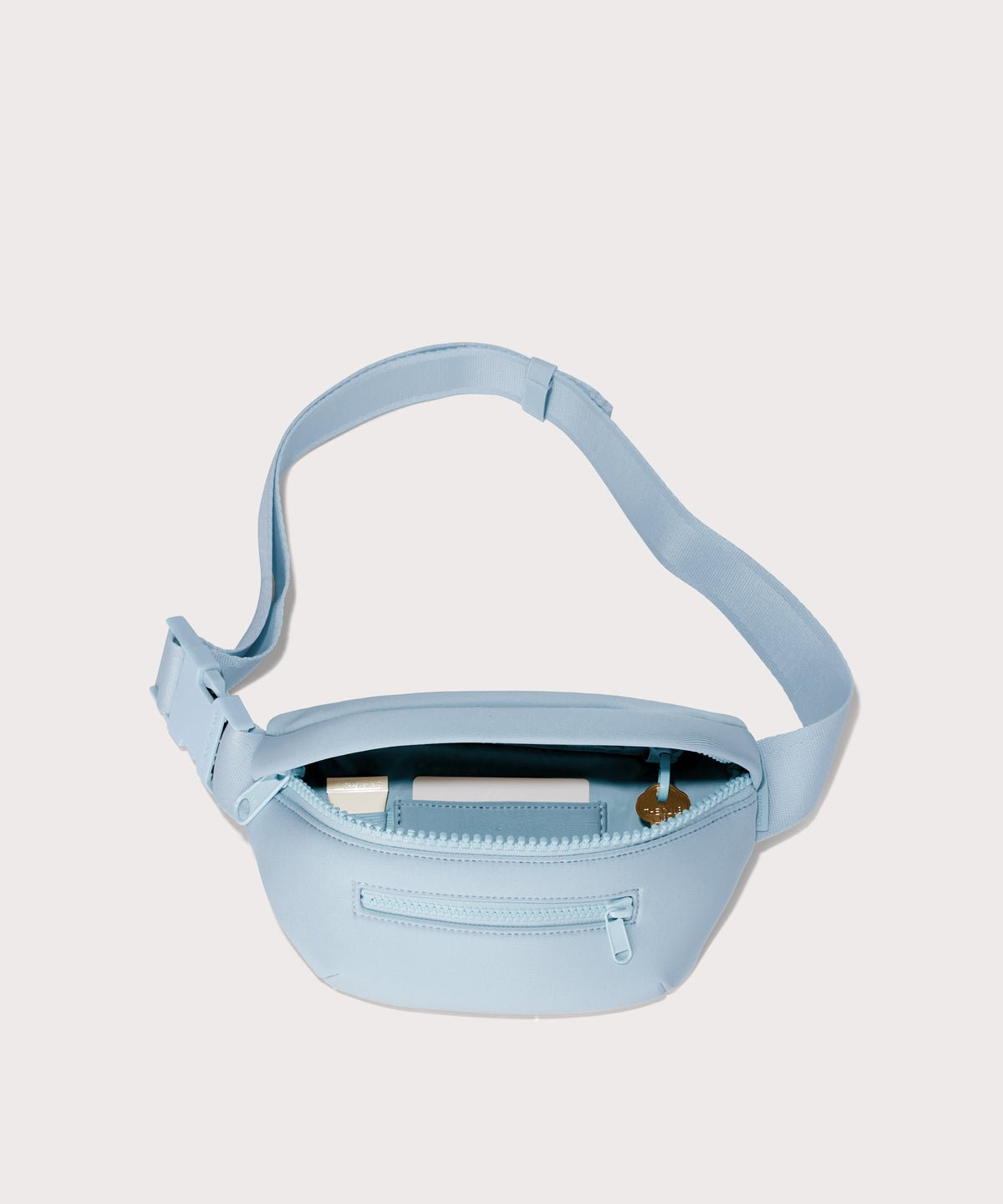 Dagne Dover Ace Fanny Pack in  an airy, lighter sky blue  unzipped, exposing the interior pockets
