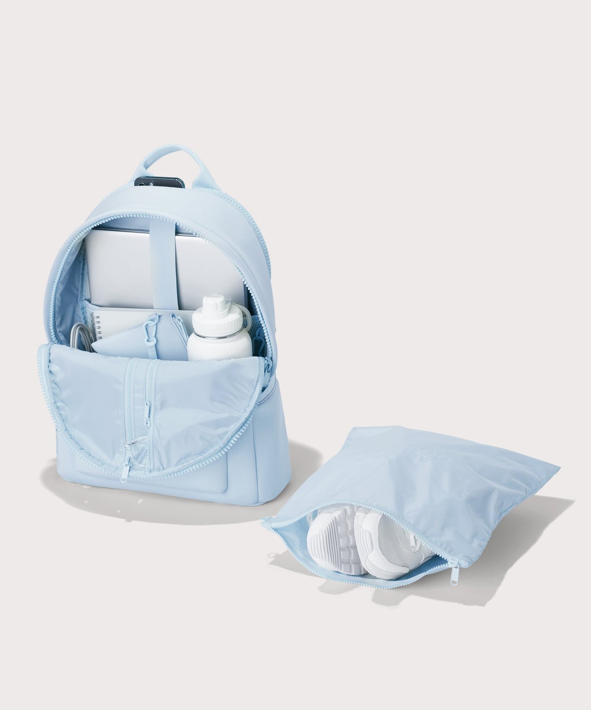 Dagne Dover large Dakota Neoprene Backpack in an airy, lighter sky blue unzipped, showing the interior pockets and shoe bag.
