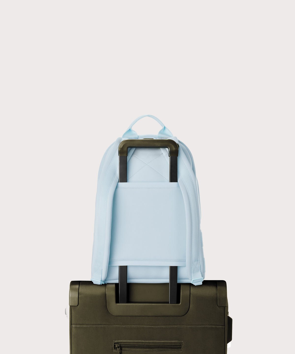 Dagne Dover medium Dakota Neoprene Backpack in an airy, lighter sky blue strapped to luggage with the neoprene luggage-handle sleeve.
