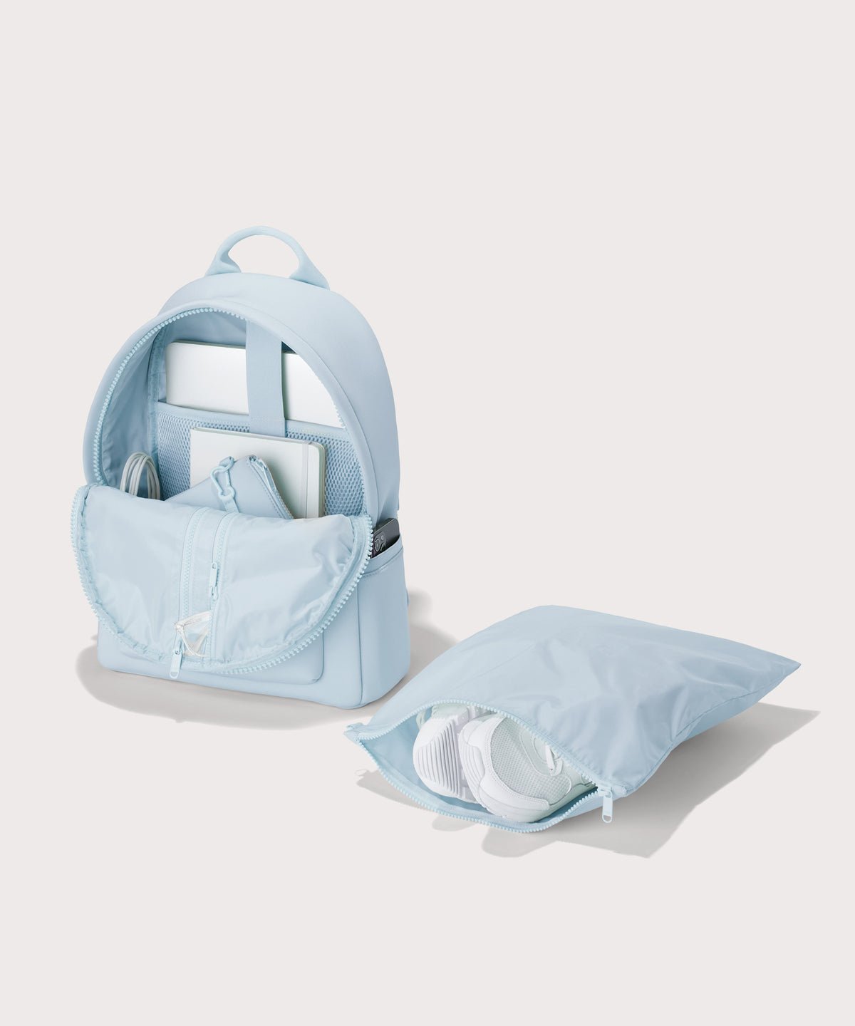 Dagne Dover medium Dakota Neoprene Backpack in an airy, lighter sky blue unzipped, showing the interior pockets and shoe bag.
