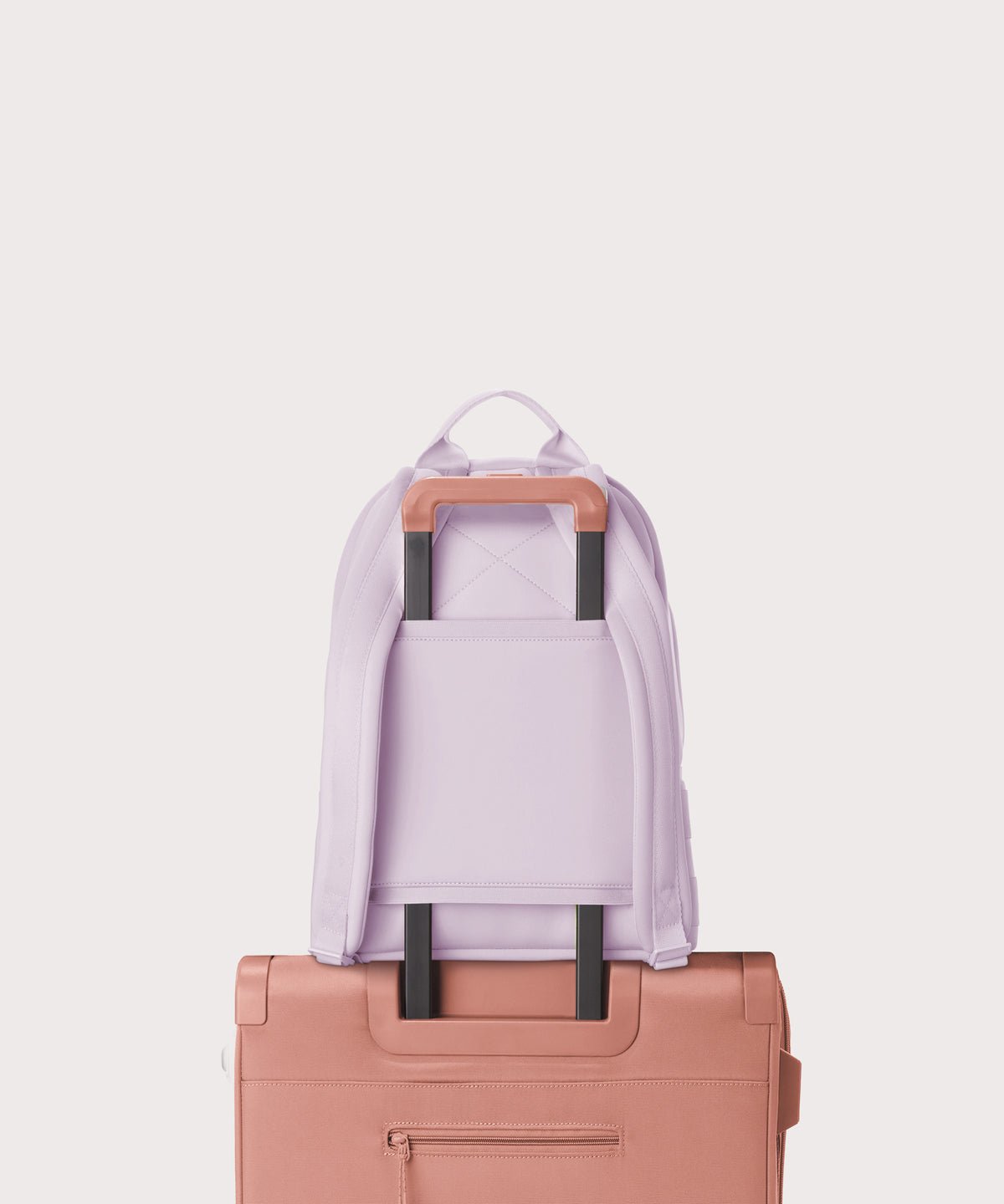 Dagne Dover medium Dakota Neoprene Backpack in a soft purple with grey undertones strapped to luggage with the neoprene luggage-handle sleeve.