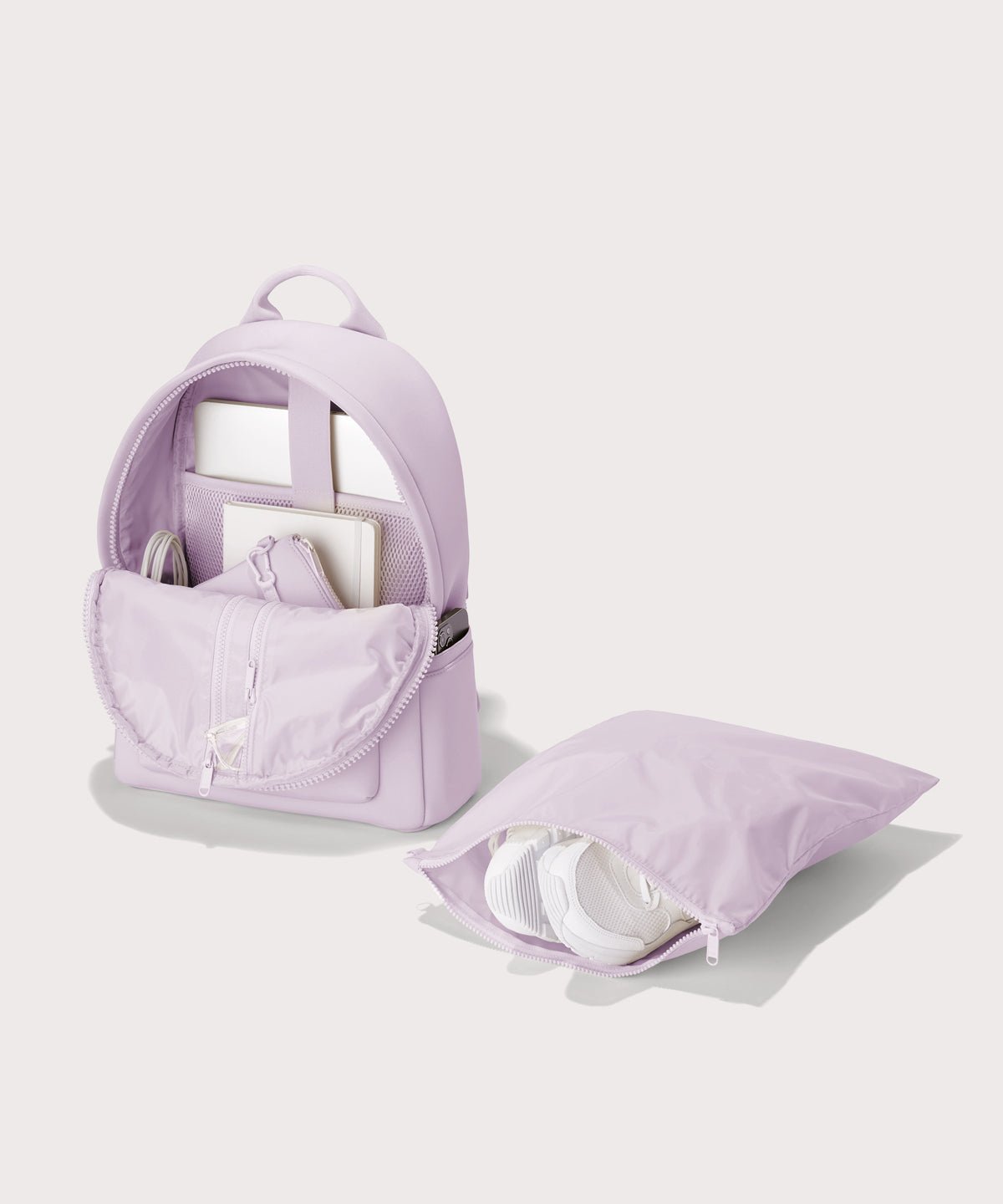 Dagne Dover medium Dakota Neoprene Backpack in a soft purple with grey undertones unzipped, showing the interior pockets and shoe bag.

