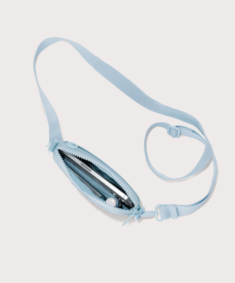 Dagne Dover Mara Phone Sling unzipped in an airy, lighter sky blue. seen from above, exposing the interior card slots.