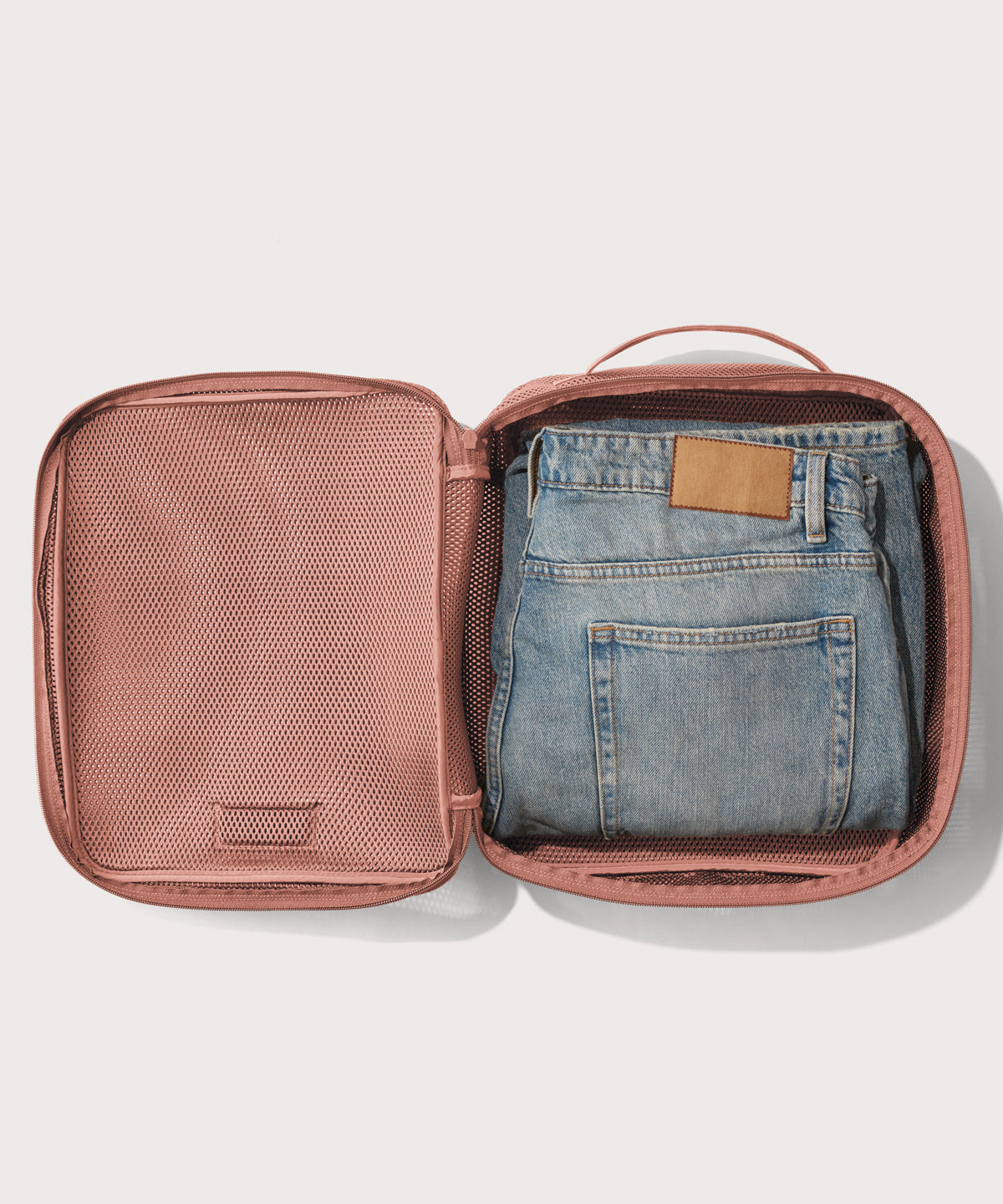 Large Roma packing cube in warm dust pink open with jeans inside
