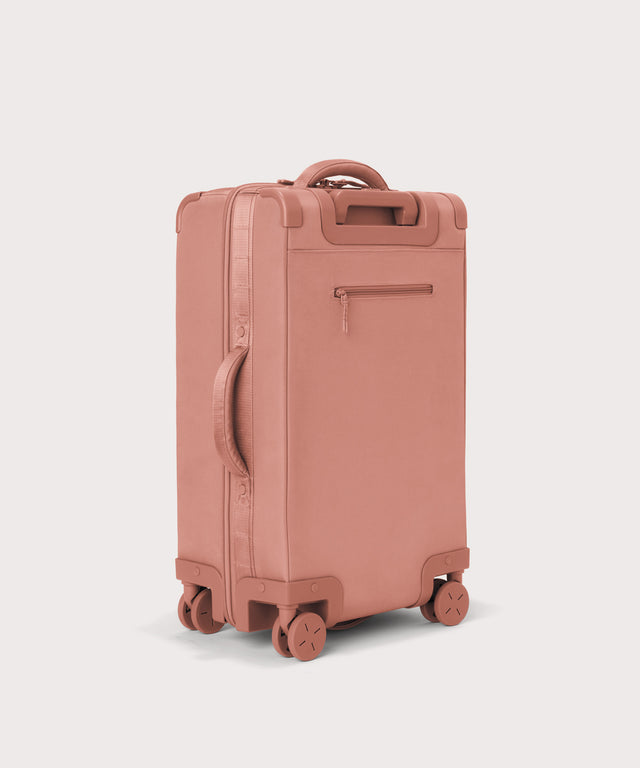 3/4 back view of Seattle carry-on rolling luggage 20.5” in warm dust pink showing side handle and back zippered phone/passport pocket

