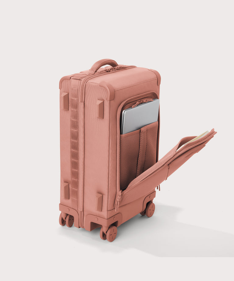¾ front view of Seattle carry-on rolling luggage 20.5” in warm dust pink with front flap opened. Caption: Interior slip pocket fits most 13" laptops
