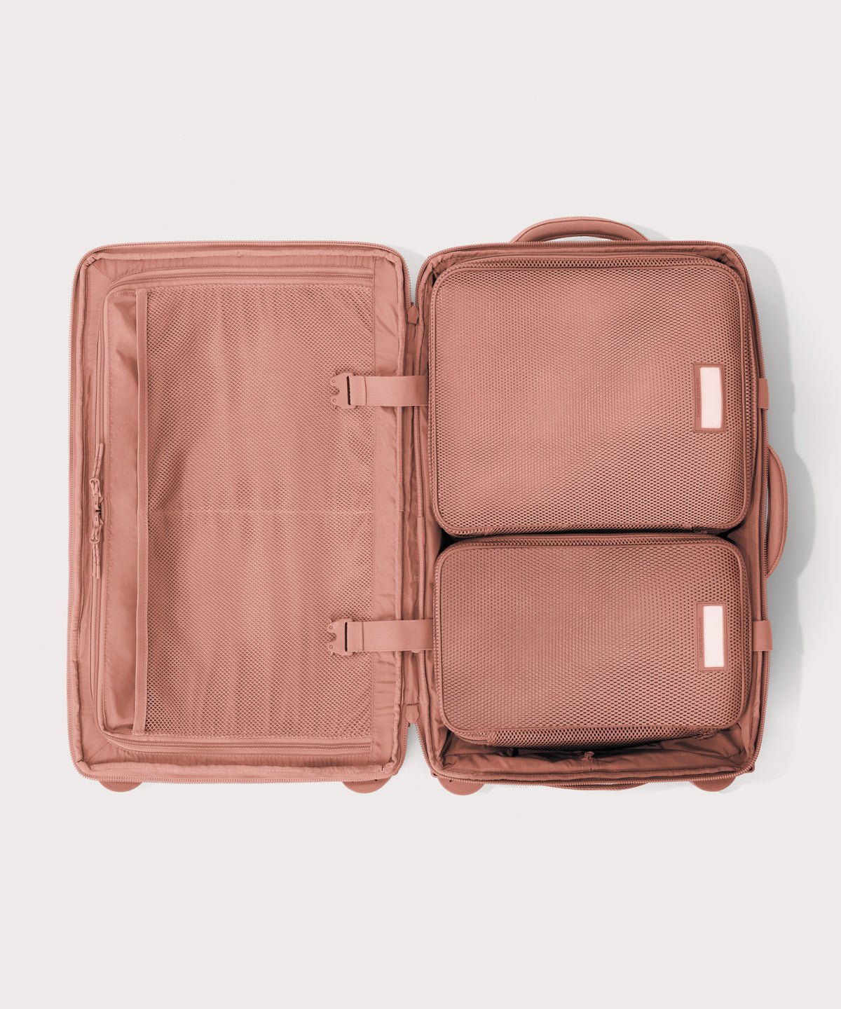 Top down of Seattle carry-on rolling luggage 20.5” in warm dust pink with interior divider zipped and packing cubes packed into the right side. 
