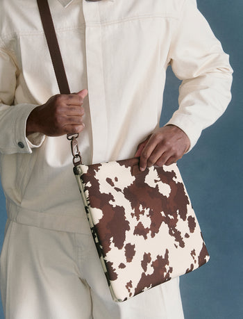Person holding a brown and cow-print bag against a blue background