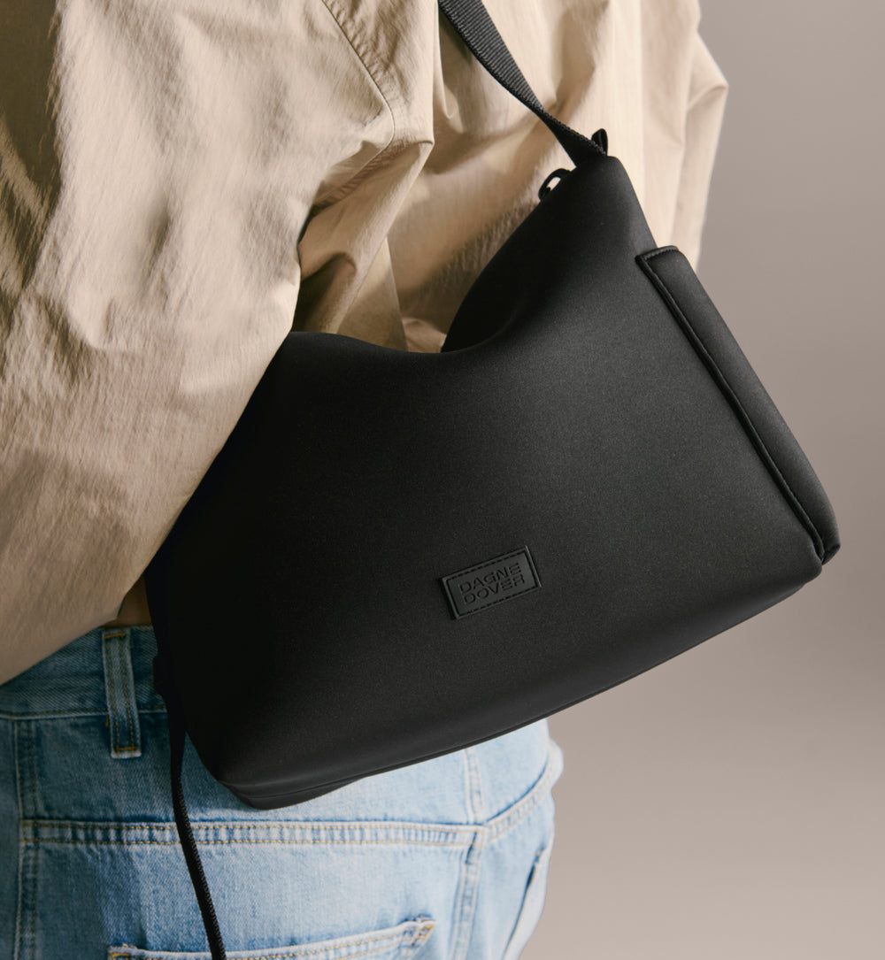 Two black handbags being held by people against a neutral background